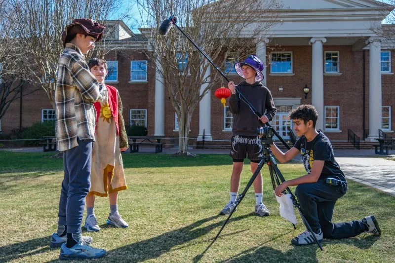 Students film a scene on the quad with a boom microphone and a camera