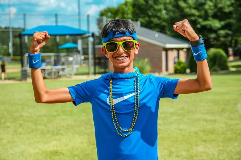 A student in sunglasses flexes and grins
