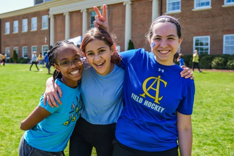 Three students hug and smile on the field