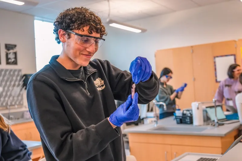 A student in lab goggles works at the bench