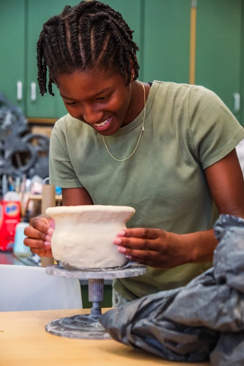 A student smiles as she shapes a bowl on the wheel