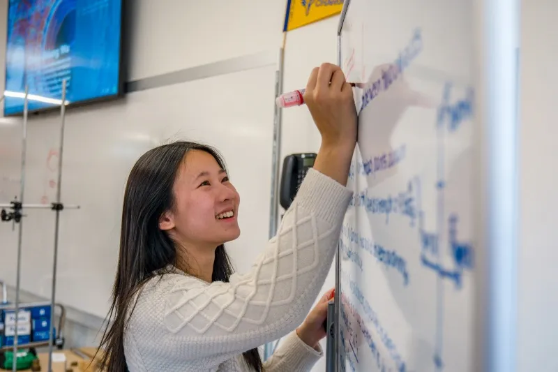 A student writes an equation on a whiteboard